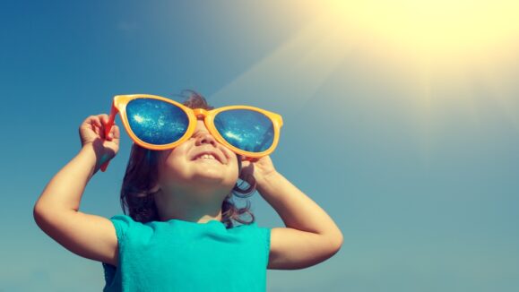 Happy little girl with big sunglasses  looking at the sun