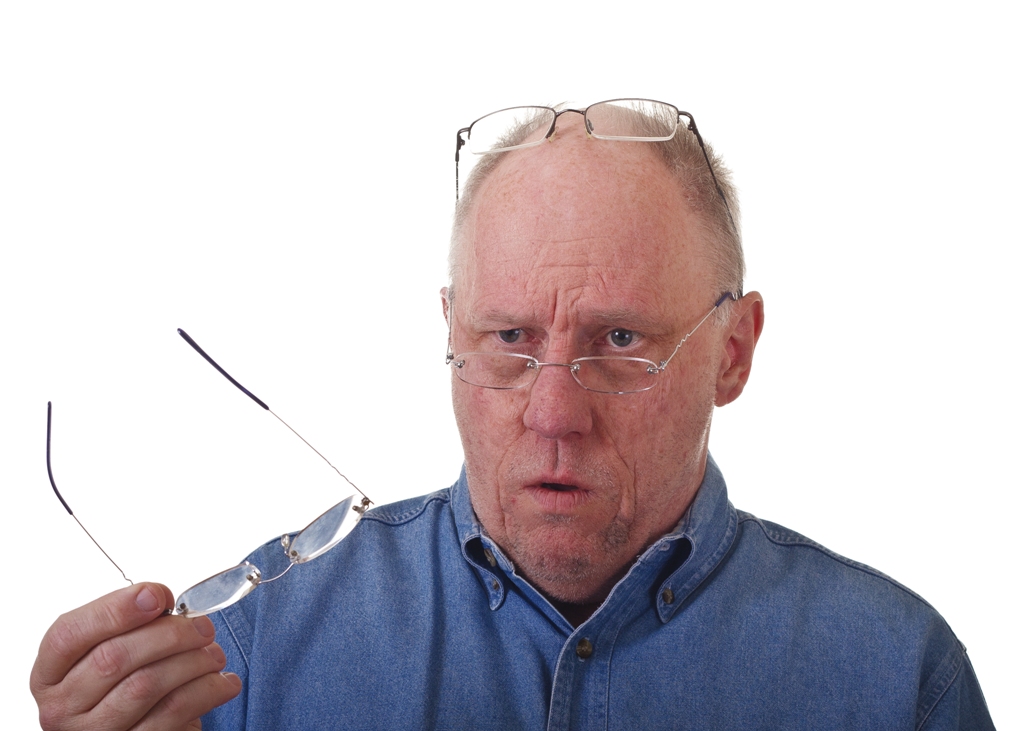 An older balding man in blue denim shirt with three pairs of reading glasses